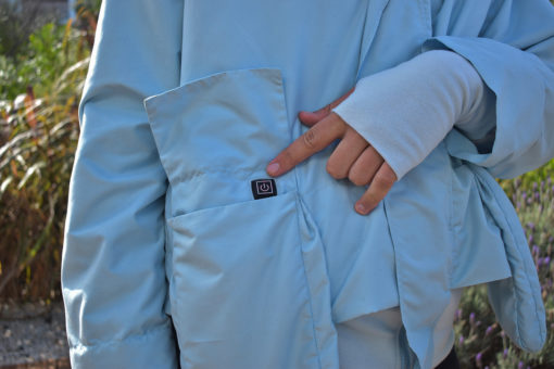 Detalle del botón de calefacción en el bolsillo de la campera impermeable celeste
